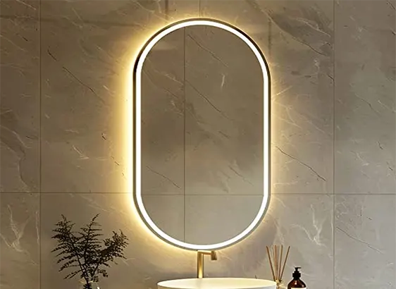 A modern, oval-shaped mirror with LED lighting is mounted on a marble wall above a bathroom sink.